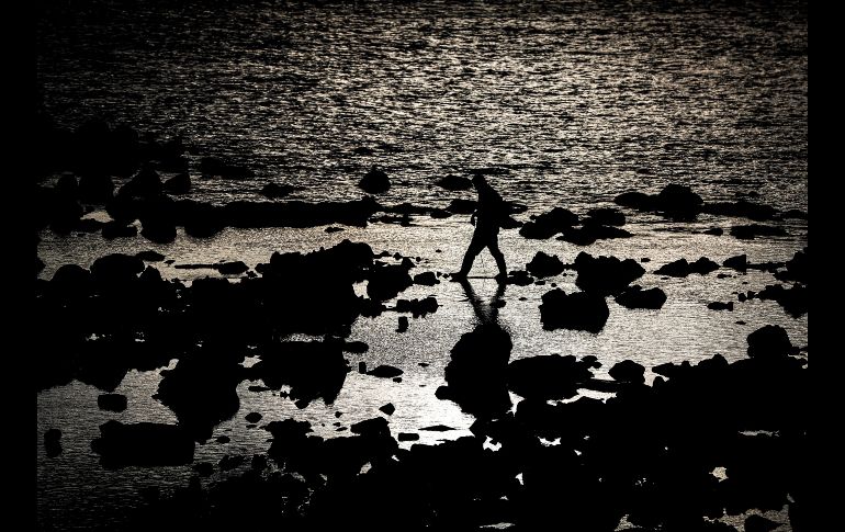 Un hombre busca crustáceos en las rocas de la playa de Ondarreta de San Sebastián, España. EFE/J. Etxezarreta.