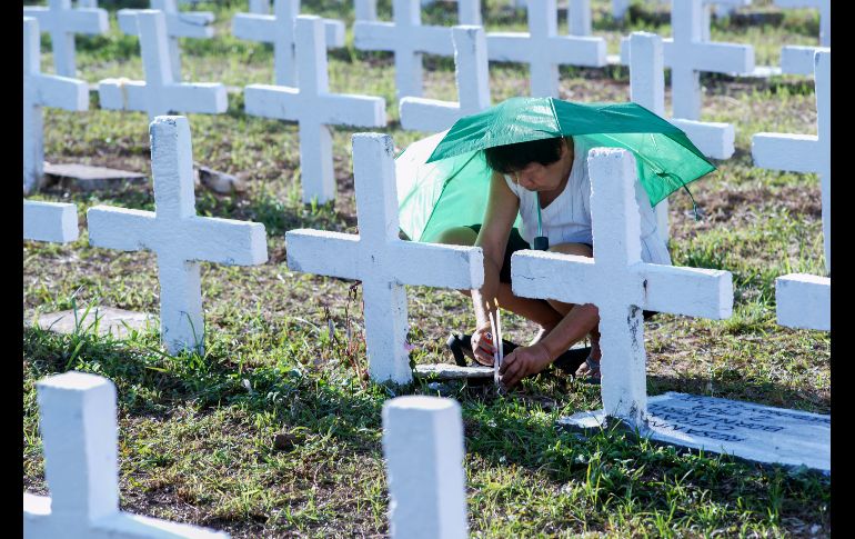 Una mujer enciende una vela por un familiar en una tumba masiva para víctimas del tifón 