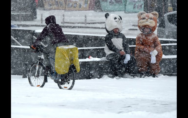 Un ciclista pasa junto a personas que llevan botargas durante una nevada, la primera del otoño, en Kiev, Ucrania. AFP/S. Supinsky