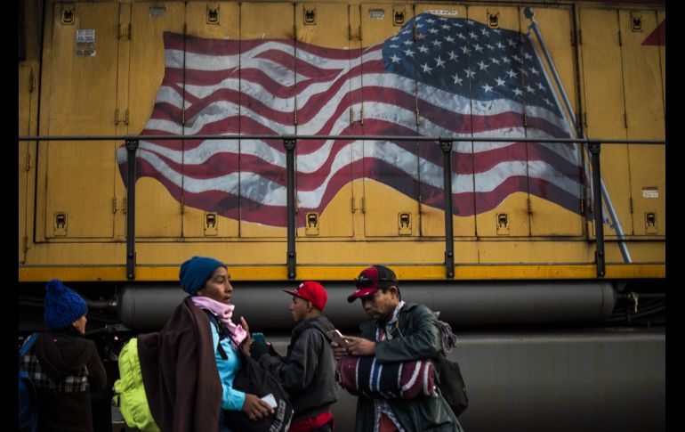 Migrantes centroamericanos se ven junto a un tren pintado con la bandera estadounidense en Mexicali, Baja California. El grupo forma parte de una caravana que se dirige a Tijuana con la intención de cruzar a Estados Unidos. AFP/P. Pardo