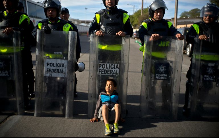 Un niño migrante descansa junto a policías. AP / R. Espinosa