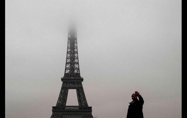Un hombre se toma una foto frente a la torre Eiffel envuelta por neblina en París, Francia. AFP/P. Lopez