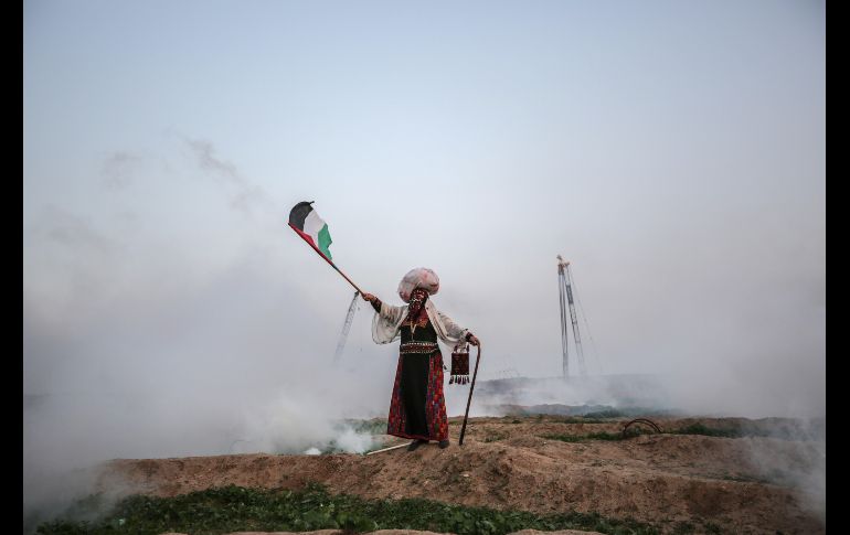 Una palestina ondea su bandera entre el gas lacrimógeno lanzado por las tropas israelíes desde la Franja de Gaza. EFE/M. Saber