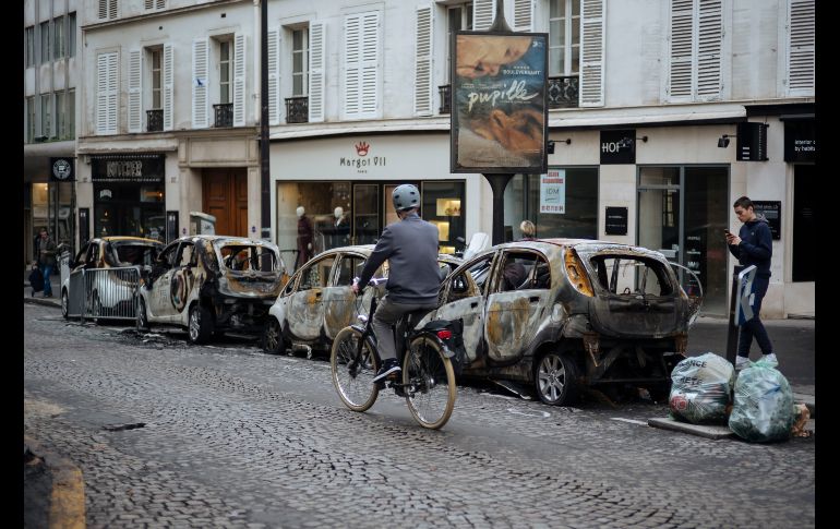 Un ciclista pasa junto a vehículos quemados en París, cerca del Arco del Triunfo, luego de que las protestas de ayer en contra del alza de impuestos se tornaron en disturbios. AP/K. Zihnioglu