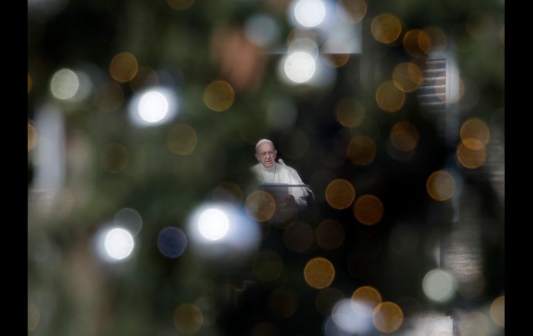 El Papa Francisco, visto entre un árbol de Navidad, habla en la oración del Ángelus desde su balcón en la Plaza de San Pedro, en el Vaticano. AP/A. Tarantino