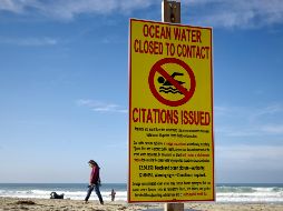 Una mujer camina hoy por la playa de  Imperial Beach, donde un letrero advierte sobre el agua contaminada. AP/G. Bull
