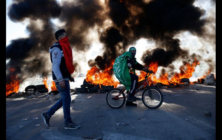 Un palestino envuelto en una bandera de Hamas se traslada en bici durante enfrentamientos con tropas israelíes en el punto de revisión de Hawara, en Cisjordania. AP/M. Mohammed