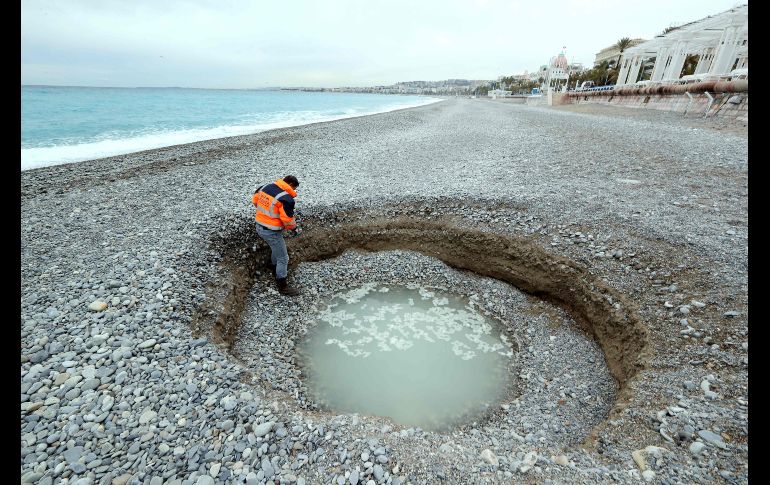 Un hombre observa el 1 de febrero un cráter de cinco metros de ancho y dos metros de profundidad que se formó en la playa Lido de Niza, en la Riviera Francesa. AFP/V. Hache