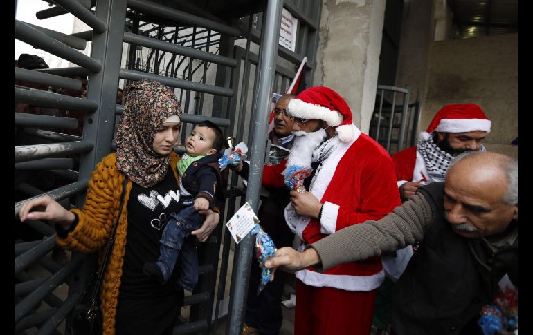 Un palestino vestido con un traje de Santa Claus le da regalos a las personas que cruzan un punto de control israelí, durante una protesta en el punto de control 300 en la ciudad cisjordana de Belén. EFE/A. Al Hashlamoun