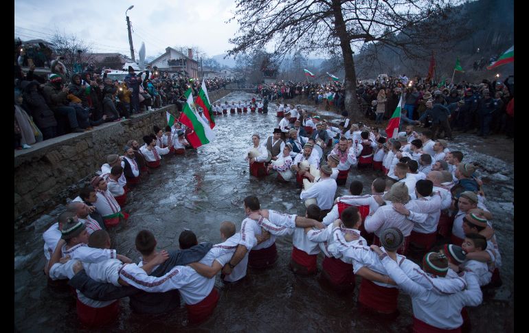 Un grupo de fieles en Kalofer, Bulgaria, acostumbra entrar al agua en atuendos tradicionales mientras ondean banderas nacionales y entonan cantos populares.
