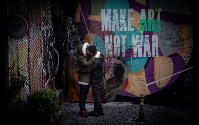 Una pareja se besa junto a un mural en el que se lee 