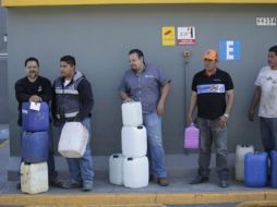 Ciudadanos esperan en una estación de servicio a surtir gasolina en recipientes de plástico; uno de ellos carga con un envase de detergente. EL INFORMADOR / F. Atilano