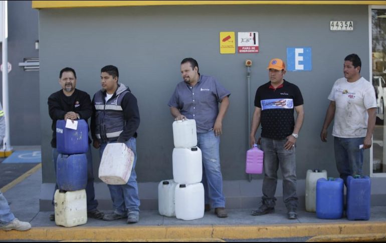 Ciudadanos esperan en una estación de servicio a surtir gasolina en recipientes de plástico; uno de ellos carga con un envase de detergente. EL INFORMADOR / F. Atilano