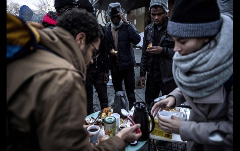 Refugiados provenientes del este de África se calientan mientras reciben alimentos de parte de voluntarios en Saint-Denis, a las afueras de París, donde viven en un campamento improvisado. AFP/C. Archambault