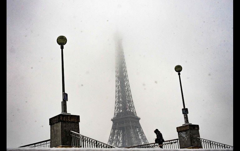 Una mujer camina por un puente que cruza el río Sena, con la torre Eiffel de fondo, durante una nevada en París. AFP/L. Bonaventure