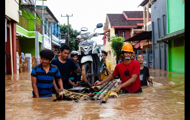 Habitantes trasladan una moto en una balsa en Makassar, Indonesia, luego de que fuertes lluvias provocaron inundaciones y aludes en la región. AFP/Y. Wahi