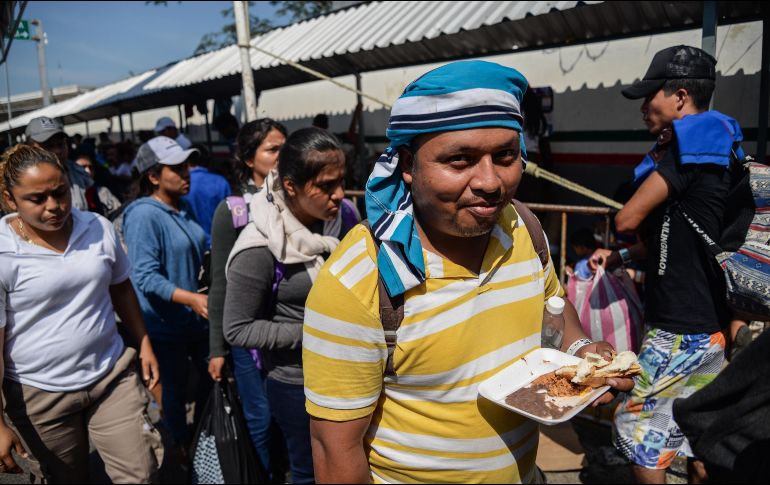 Migrantes hondureños comen mientras continúan con los trámites para obtener la tarjeta humanitaria del Instituto Nacional de Migración. EFE/L. Villalobos