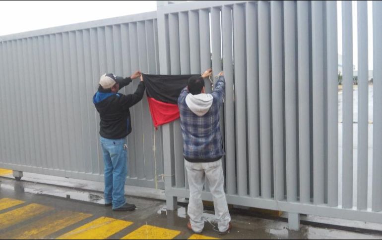 Empleados retiran una bandera rojinegra colocada a la entrada de una fábrica. TWITTER