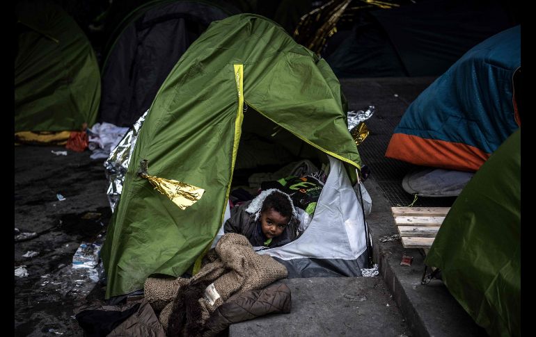 Un niño se asoma de una casa de campaña en un campamento improvisado para migrantes en la zona de  Porte de la Chapelle, París, en el marco de un operativo para evacuar el sitio y enviar a los migrantes a refugios en gimnasios cercanos. AFP/C. Archanbault