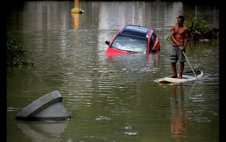Un hombre se transporta en una tabla de paddle surf por una zona inundada por la fuerte tormenta en el barrio de Barra da Tijuca.