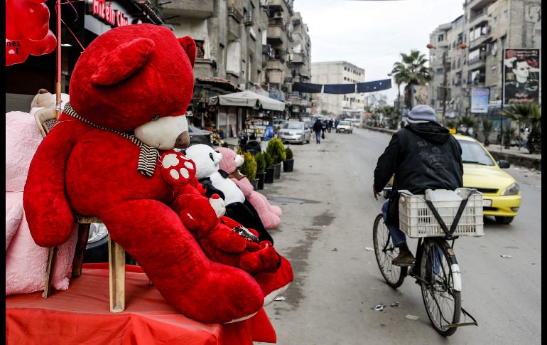 Un ciclista pasa junto a un oso de San Valentín en una calle de Jaramana, Siria. AFP/L. Beshara