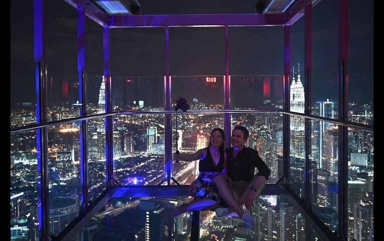 Una pareja se toma selfies en una caja de cristal en un mirador de Kuala Lumpur, Malasia. AFP/M. Rasfan