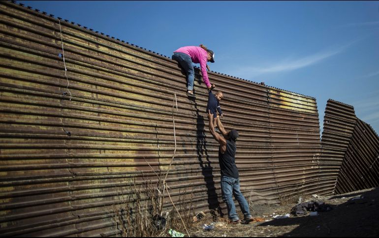 La fotografía muestra una familia de migrantes latinoamericanos que escalan una valla entre México y Estados Unidos. AFP/ Pedro Pardo