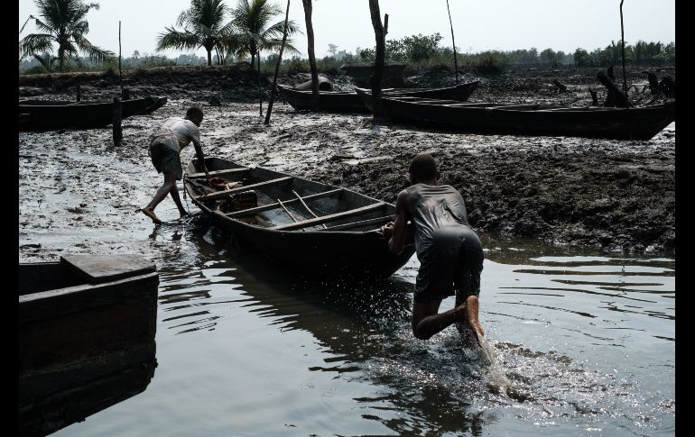 Pescadores empujan su bote durante la marea baja en un río en la población nigeriana de K-Dere. Según el Movimiento para la Supervivencia del Pueblo Ogoni, el río ha sido contaminado por constantes derrames de petróleo desde los años 1970. AFP/Y. Chiba