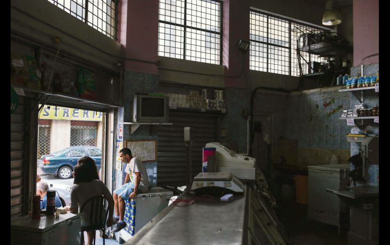 Tres personas esperan en la entrada de una carnicería localizada en la capital de Venezuela. AFP