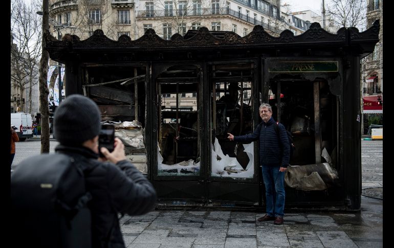 Un hombre posa este domingo para una foto frente a un kiosko dañado durante las protestas del sábado.