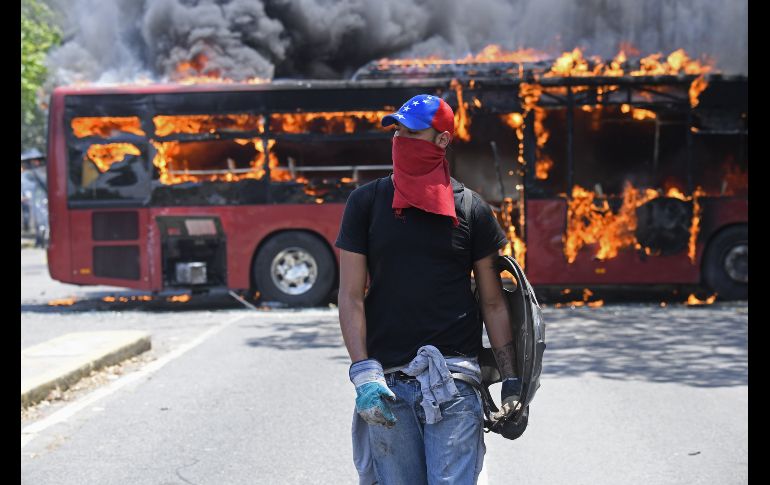 Un manifestante camina frente a un autobús incendiado durante los enfrentamientos en los alrededores de La Carlota. AFP/F. Parra