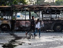 Personas pasan  junto a un autobús calcinado, luego de los enfrentamientos de ayer en Caracas. AFP/M. Delacroix
