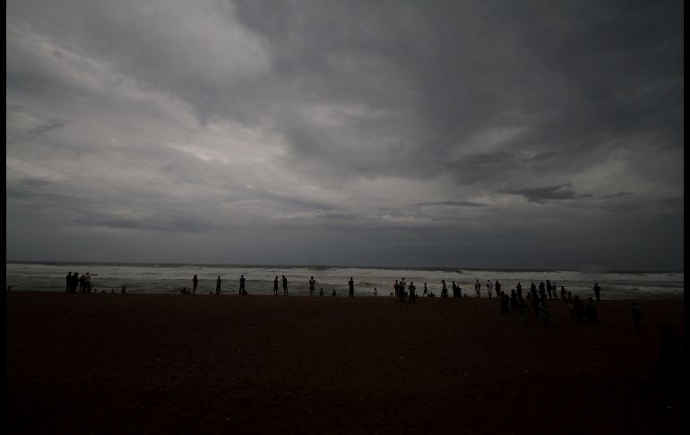 Personas contemplan el oleaje bajo nubes oscuras en la costa de Puri, donde se espera que 