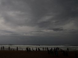 Personas contemplan el oleaje bajo nubes oscuras en la costa de Puri, donde se espera que 