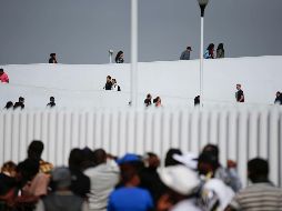 Personas cruzaban ayer (arriba) de Tijuana, Baja California, hacia Estados Unidos, mientras migrantes (abajo) aguardaban para pedir asilo. AP/ARCHIVO