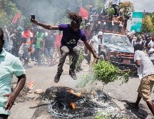 Un hombre salta por encima de un neumático en llamas, este domingo, durante una manifestación para exigir la dimisión del presidente haitiano, en Puerto Príncipe. EFE/J. Herve