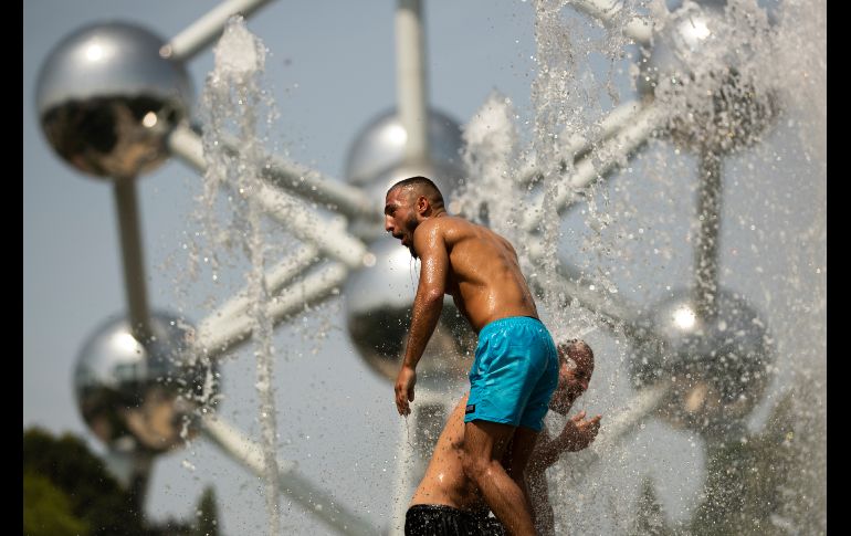 Hombres se refrescan en una fuente pública cerca del Atomium en Bruselas, Bélgica