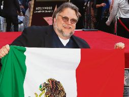 Guillermo del Toro se ve sonriente, mientras arrodillado y con la bandera posa para los camarógrafos. AP