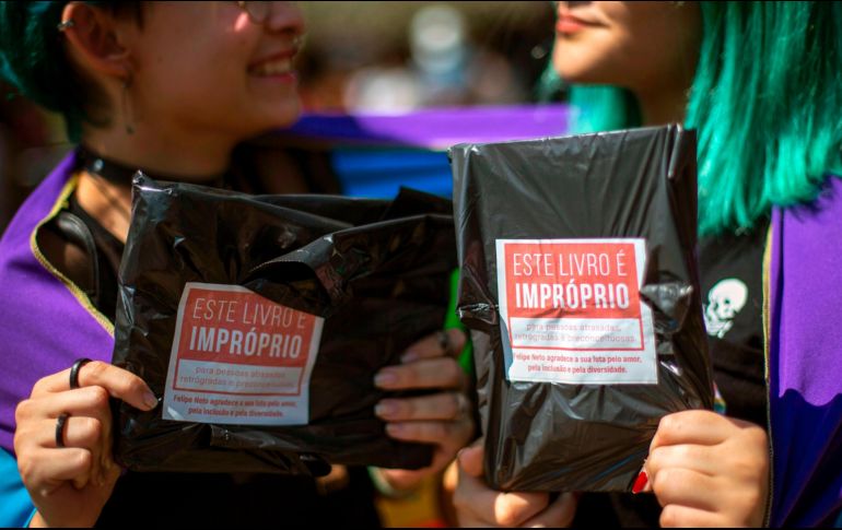 Mujeres muestran dos de los 14 mil libros de temas LGBT comprados y regalados en la bienal de Río de Janeiro por el youtuber Felipe Neto, en protesta contra la censura del alcalde.  AFP/Bienal do Livro do Rio