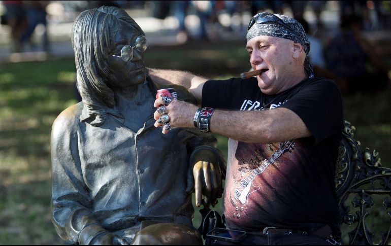 Un fanático de la banda británica The Beatles fuma un puro y brinda con cerveza junto a una estatua de John Lennon. EFE/Y. Zamora