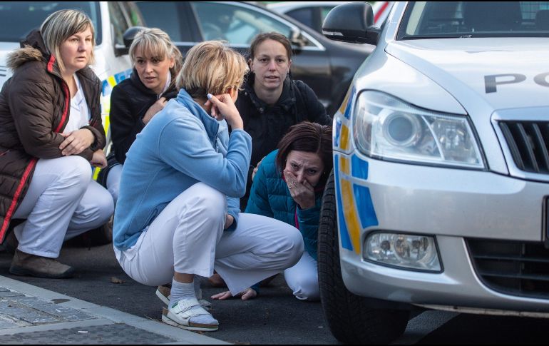 Varias enfermeras se esconden detrás de un coche de policía mientras los agentes persiguen al autor del tiroteo en el hospital de Ostrava. EFE/L. Kabon