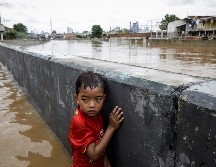 Un niño se protege tras un muro en una carretera inundada de Yakarta. EFE/M. Irham