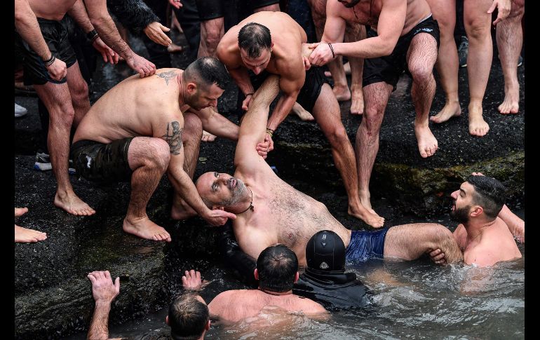 En Estambul, Turquía, personas ayudan a un hombre que se sintió mal tras sumergirse en las aguas frías de un río. AFP/O. Kose