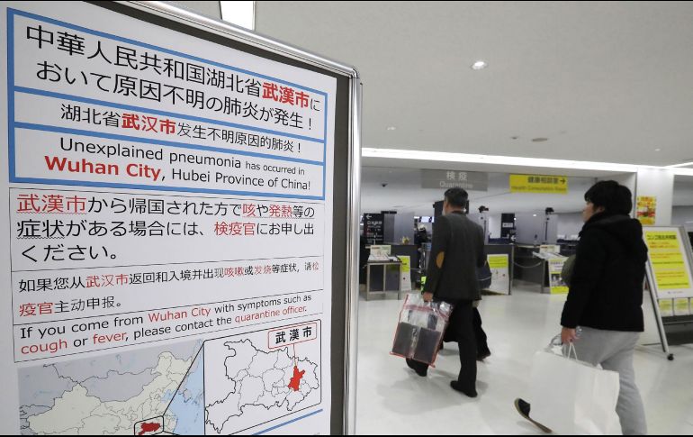 Pasajeros pasan junto a un letrero de advertencia sanitaria en el aeropuerto de Narita, en la prefectura de Chiba. AFP/JIJI PRESS