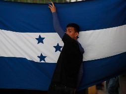 Un migrante sostiene una bandera de Honduras mientras espera junto al río Suchiate, en Chiapas. AP/M. Castillo