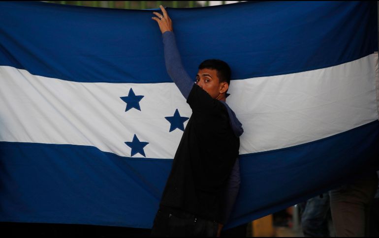 Un migrante sostiene una bandera de Honduras mientras espera junto al río Suchiate, en Chiapas. AP/M. Castillo