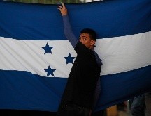 Un migrante sostiene una bandera de Honduras mientras espera junto al río Suchiate, en Chiapas. AP/M. Castillo