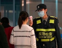 Personal del aeropuerto en Wuhan, China, checa la temperatura de pasajeros como parte de las medidas para frenar el brote del coronavirus. AP/D. Kang