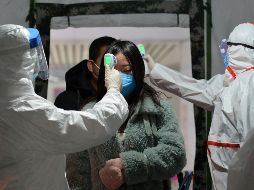 Trabajadores de la salud toman la temperatura a una pasajera en la estación de trenes de Fuyang, China. AP