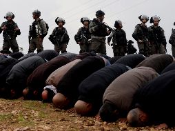 Varios soldados israelíes contemplan a un grupo de palestinos que rezan durante una protesta en la ciudad cisjordana de Tubas. EFE/A. Badarneh